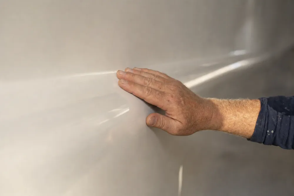 A hand running along a finished, glossy white hull to check it by feel