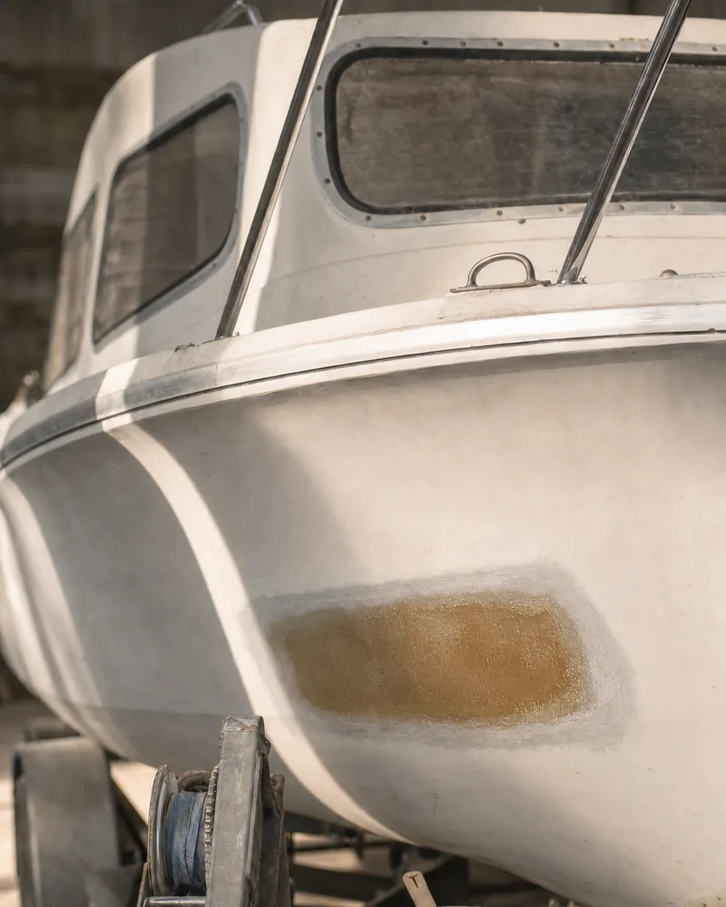 A small cabin cruiser on its trailer with fresh fibreglass laminated into a repair on the bow, resin cup and roller beside it